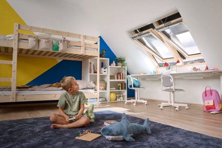 Chlapec v podkrovnej detskej izbe s moderným nábytkom a otvorenými oknami Velux.
