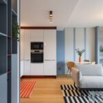 Denná miestnosť s bielou linkou, bordovým soklom, modrou policovou stenou a farebným pruhovaným kobercom na drevenej podlahe.