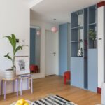 Pohľad na chodbu s modrou vstavanou skriňou, fialovými stoličkami s rastlinou a moderným čierno-bielym kobercom.