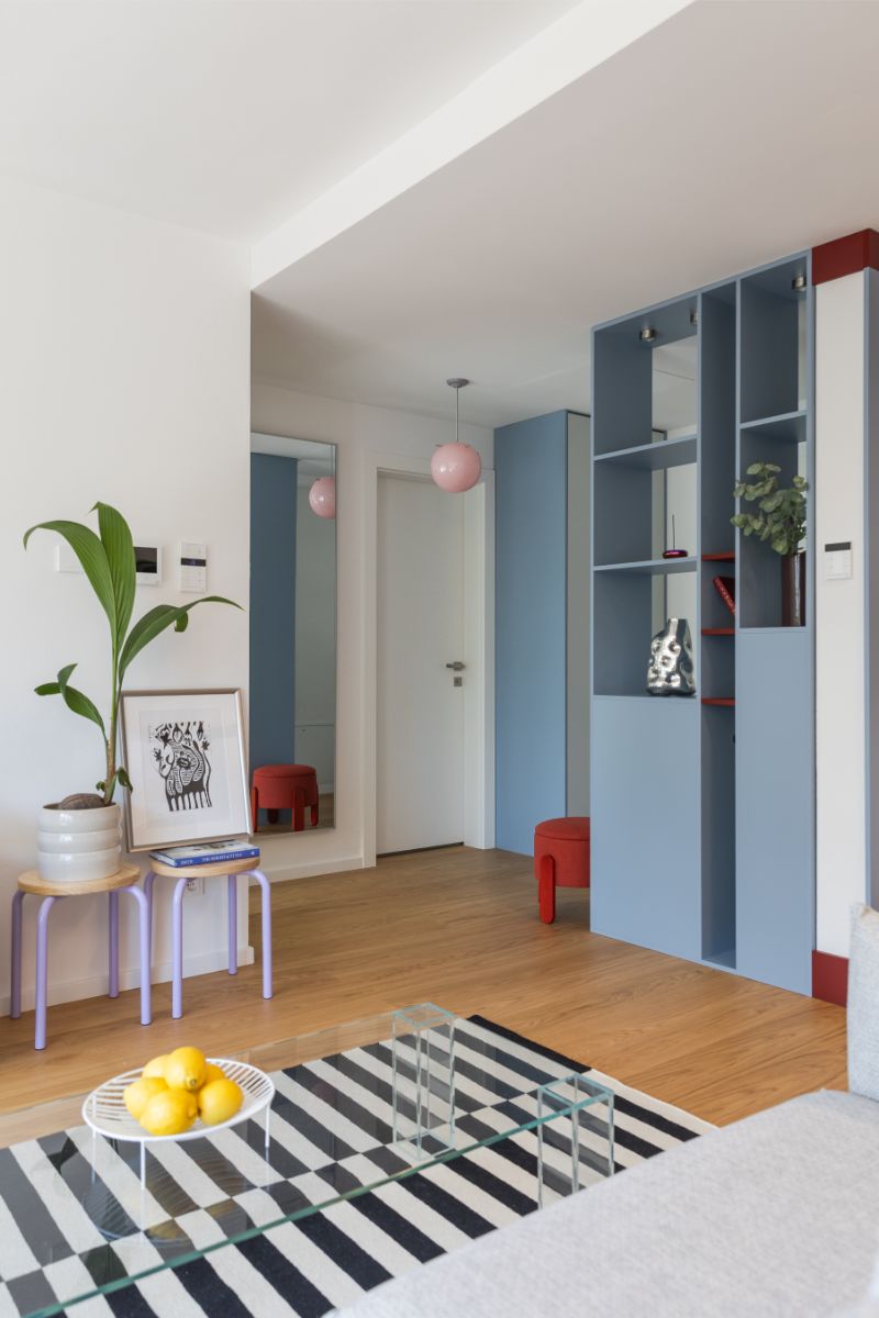Pohľad na chodbu s modrou vstavanou skriňou, fialovými stoličkami s rastlinou a moderným čierno-bielym kobercom.