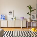 Obývacia izba s modrou pruhovanou stenou, bielou knižnicou, oranžovým kreslom a okrúhlym jedálenským stolom.