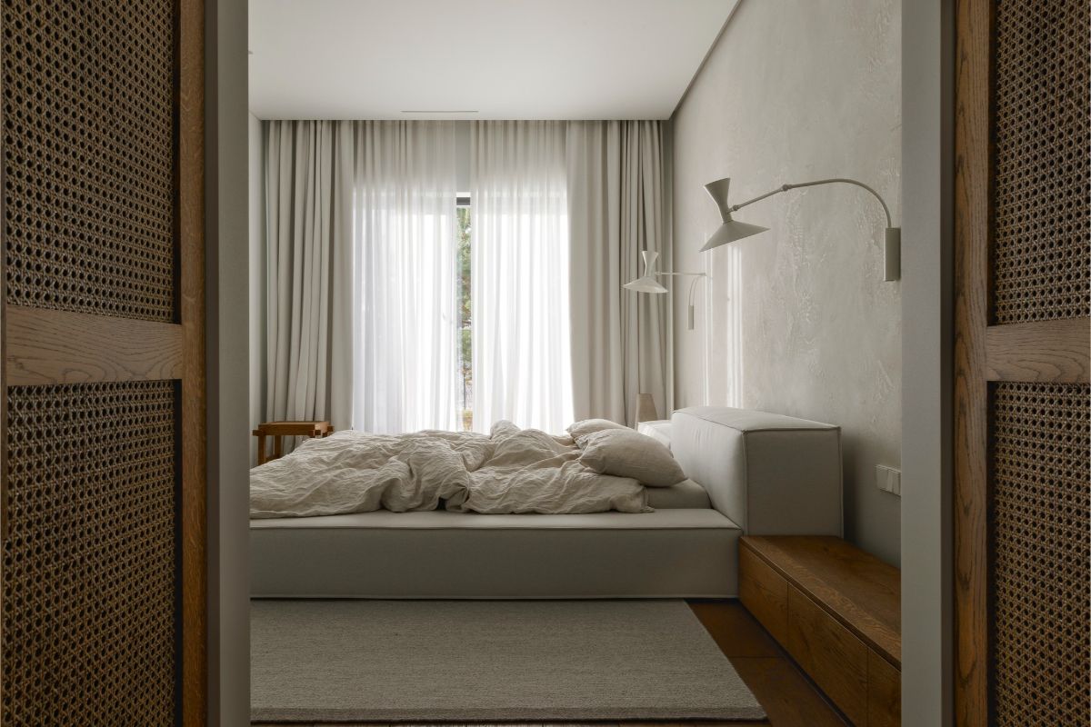 Svetlá spálňa s nízkou čalúnenou posteľou, ľanovou posteľnou bielizňou a minimalistickými bielymi nástennými lampami.