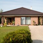 Moderný bungalov so stanovou strechou, krýtou terasou a tehlovou fasádou.