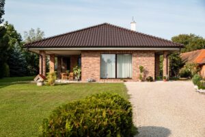 Moderný bungalov so stanovou strechou, krýtou terasou a tehlovou fasádou.