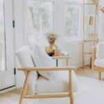 bývacia izba so svetlým textilným kreslom, drevenou konštrukciou, zlatou vázou so suchými kvetmi a bielym pleteným kobercom.