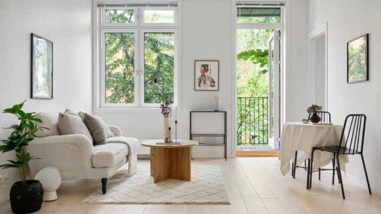 Obývacia izba s bielou klasickou pohovkou, okrúhlym dreveným stolom a čiernym kovovým jedálenským setom.