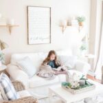 Obývacia izba s bielou látkovou sedačkou, prútenými kreslami a svetlým dreveným citátom na stene.