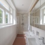 Kúpeľňa s terakotovou dlažbou, bielym dvojumývadlom, preskleným sprchovacím kútom a veľkým zrkadlom.