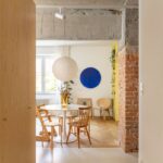 Jedáleň s bielym kruhovým stolom, drevenými stoličkami, priznaným betónovým stropom a červeným tehlovým stĺpom.