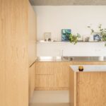 Kuchynská linka so svetlým dreveným dekorom, nerezovým drezom, kovovou policou a modernými abstraktnými obrazmi.