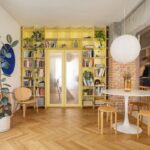 Jedáleň so žltou policovou stenou, bielym jedálenským stolom, drevenými taburetkami a parketami so vzorom stromčeka.