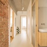 Chodba so svetlou podlahou, drevenými zárubňami, presklenými dverami do kúpeľne a surovým betónovým stropom.