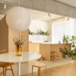 Kuchyňa spojená s jedálňou, dreveným ostrovom, bielym dizajnovým stolom a veľkým papierovým svietidlom.