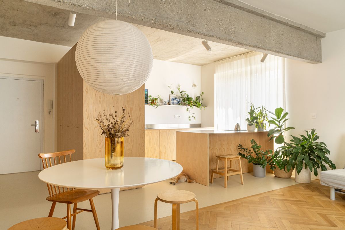 Kuchyňa spojená s jedálňou, dreveným ostrovom, bielym dizajnovým stolom a veľkým papierovým svietidlom.