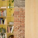 Pohľad na drevený obklad, tehlovú stenu a žltú knižnicu.