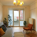 Obývacia izba s pôvodnými parketami, retro oranžovým kreslom, sivou pohovkou a klasickými balkónovými dverami.