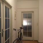 Predsieň s laminátovou podlahou, bielymi stenami, presklenými interiérovými dverami a zaparkovaným mestským bicyklom.