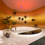 Kúpeľňa s vírivkou, zlatým lamelovým obkladom, červeným stropným svetlom a visiacou interiérovou zeleňou.