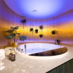 Kúpeľňa s vírivou vaňou, zlatou stenou, modrým LED podsvietením a čiernym odkladacím pultom.