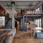 Otvorený loft s drevenou parketovou podlahou, kovovým schodiskom, čiernou oceľovou galériou a bielym rebrovaným stropom.