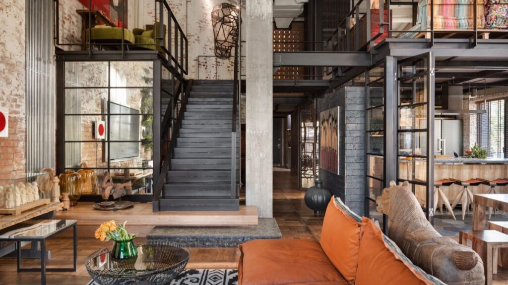 Loftový byt s presklenými oceľovými priečkami, tehlovou stenou, zaradením obývačky a kuchyne a schodiskom na galériu s oceľovým zábradlím.