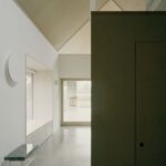 Svetlá chodba s leštenou betónovou podlahou, minimalistickou drevenou stenou a vysokým preglejkovým stropom.