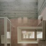 Kúpeľňa s ružovým obkladom, svetlým dreveným oknom a sivým pohľadovým betónom na strope.