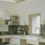 Kuchyňa so svetlou preglejkovou linkou, čiernym mramorovým obkladom a bielym keramickým drezom.