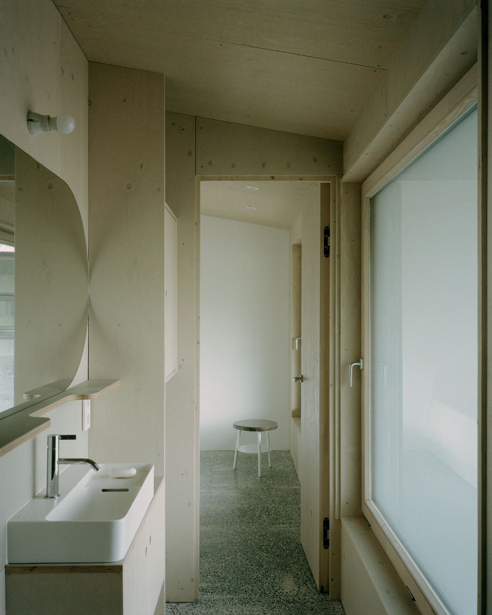 Chodba so svetlým dreveným obkladom, brúsenou betónovou podlahou a bielym keramickým umývadlom.