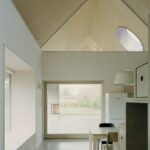 Moderná kuchyňa s bielym nábytkom, svetlým dreveným jedálenským stolom a okrúhlym strešným oknom.