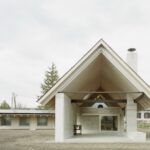 Moderná jednopodlažná stavba s vysokou sedlovou strechou a presklenou stenou s posuvnými dverami a terasou.