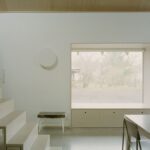 Presvetlená jedáleň s veľkým oknom, nízkou drevenou komodou a minimalistickým bielym svietidlom.