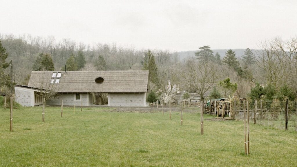 Moderný rodinný dom so sivou kamennou fasádou, tradičnou drevenou strechou a rozľahlou trávnatou lúkou.