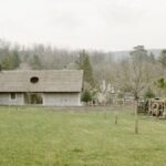 Moderný rodinný dom so sivou kamennou fasádou, tradičnou drevenou strechou a rozľahlou trávnatou lúkou.