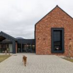 Moderný členitý dom s tehlovou a čierno plechovou fasádou.