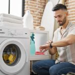 Muž kľačí pri práčke a pozerá sa na hodinky.