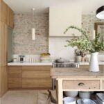 Kuchyňa s kamenným obkladom steny, svetlou drevenou linkou a rustikálnym ostrovom s bielou keramikou.