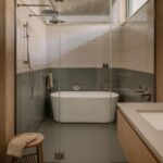 Kúpeľňa so skleneným sprchovacím kútom, bielou voľne stojacou vaňou a vertikálnym krémovým obkladom.