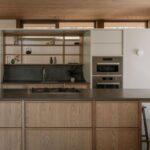 Kuchyňa s dreveným ostrovom, tmavou pracovnou doskou, vstavanými antikorovými rúrami a policami z vlnitého skla.