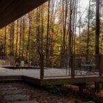 Vonkajšia drevená terasa s bazénom, kovovým zábradlím a výhľadom na les.