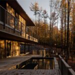 Dvojpodlažná chata s hnedým dreveným fasádnym obkladom, bazénom na terase a kamenným oporným múrom.