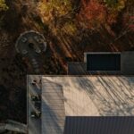 Pohľad zhora kolmo na zem na plechovú strechu domu a ohnisko vedľa neho v lese.