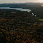 Letecký pohľad na rozsiahly jesenný les s modrým jazerom, kľukatou riekou a vzdialenými horskými masívmi.