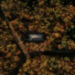 samotený dom so sivou plechovou strechou uprostred hustého jesenného lesa s oranžovým a zeleným lístím.