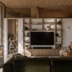 Obývacia izba s drevenou knižnicou, moderným bielym krbom, olivovozelenou sedačkou a veľkoformátovým presklením.