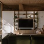 Obývacia izba s dubovým policovým systémom, čiernym televízorom, koženým kreslom a svetlým dreveným stropom.