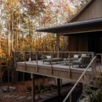 Drevená terasa s kovovým zábradlím, olivovozeleným exteriérovým nábytkom a výhľadom na okolité farebné stromy.