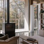 Obývacia izba s čiernou krbovými kachľami, nízkym dreveným stolíkom a veľkoformátovým oknom do lesa.