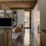 Interiér s leštenou betónovou podlahou, koženým hnedým kreslom a svetlou drevenou knižnicou.