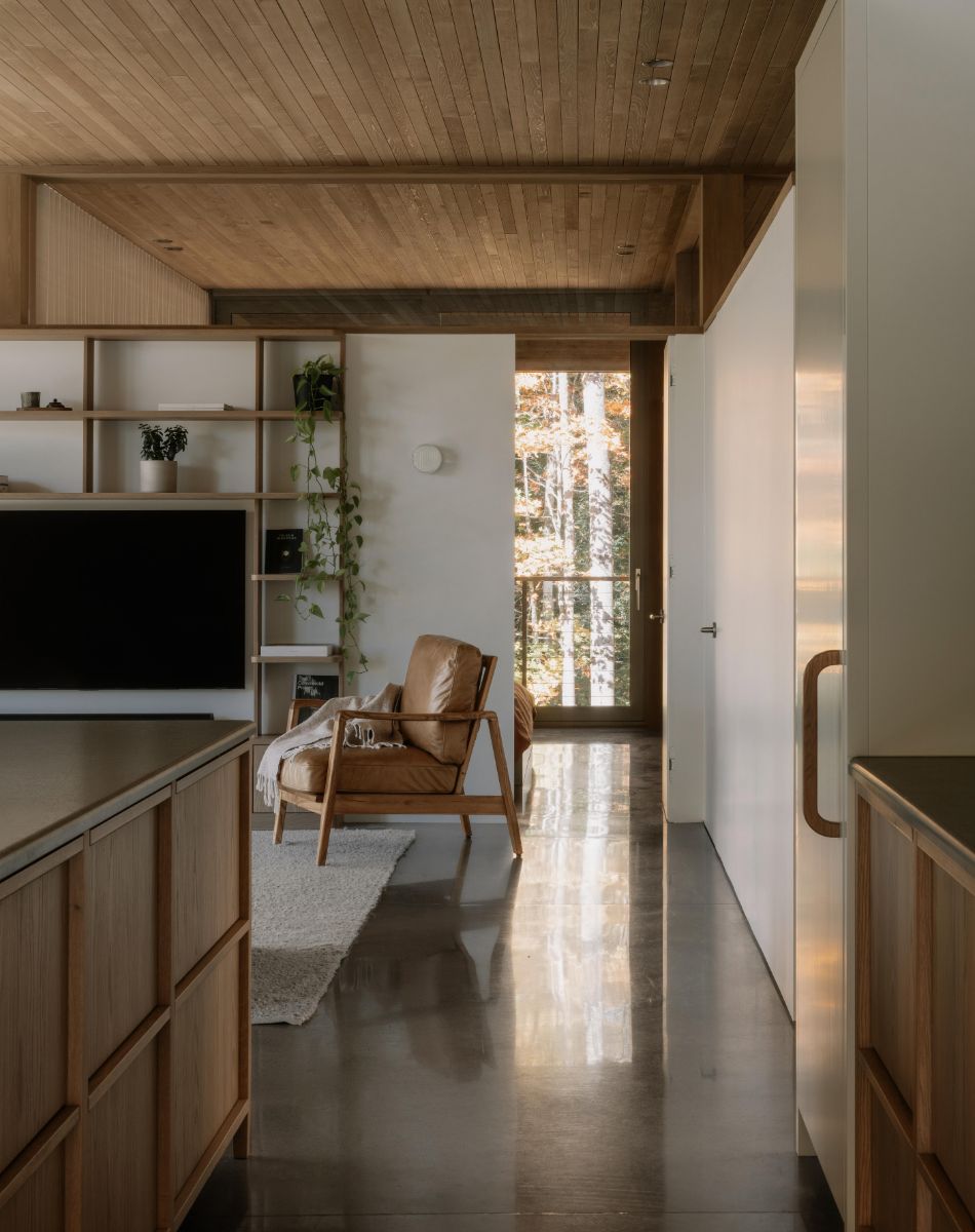 Interiér s leštenou betónovou podlahou, koženým hnedým kreslom a svetlou drevenou knižnicou.